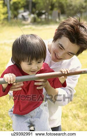 Stock Image - Father lifts up his son for holding a metallic rod. Fotosearch