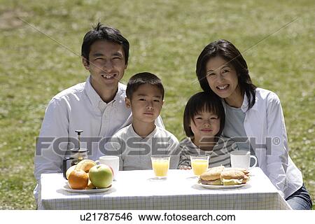 Stock Photograph - Portrait of a family smiling in garden by breakfast table. Fotosearch
