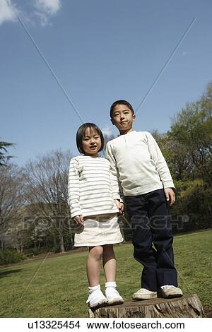 Picture - Portrait of children standing on wooden log in garden. Fotosearch