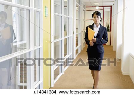 Picture - A businesswoman holding a file walks along the passage of the office. Fotosearch