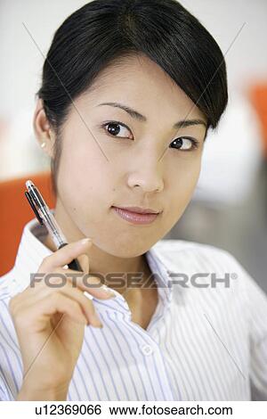 Stock Photograph - A businesswoman holding a pen lost in her thoughts. Fotosearch
