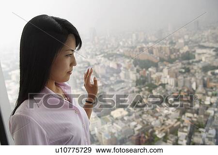 Stock Photo - A formally dressed woman stands against the window lost in her thoughts. Fotosearch