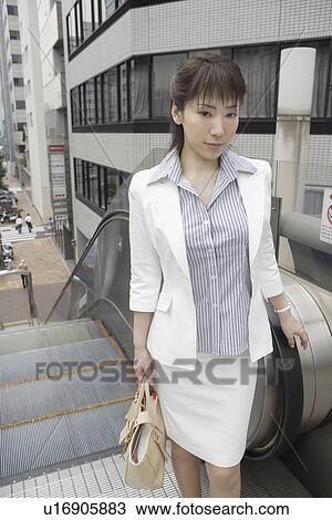 Stock Image - A formally dressed woman stands near the escalators. Fotosearch