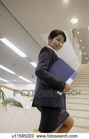 Stock Image - A professional woman holding a file climbs the staircase. Fotosearch