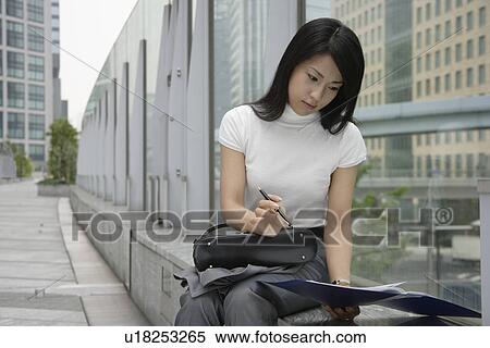 Stock Photography - A woman holding a pen looks over the documents in a file. Fotosearch