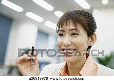 Stock Photo - A woman holding a pen smiles at someone. Fotosearch