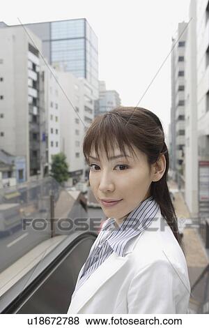 Stock Photo - A woman looking at the camera as a commercial area is seen at the back. Fotosearch