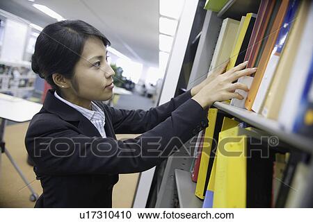 Stock Image - A woman looks over the shelf containing various files. Fotosearch