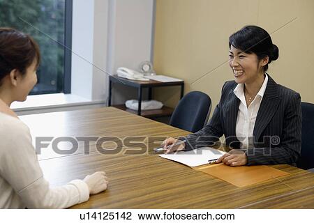 Stock Image - Two professional women sharing laughter in the office. Fotosearch