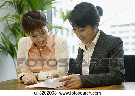 Stock Photo - Two woman express happiness as they look over the sheet of the file. Fotosearch