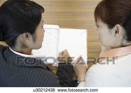 Stock Photograph - Two women exchanging views as the have a look over the papers. Fotosearch