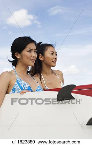 Stock Image - Close-up of young women standing with surfboards. Fotosearch