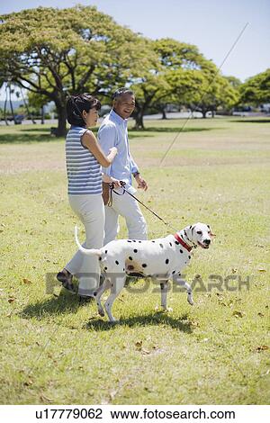 Stock Image - Husband and wife walking with dog. Fotosearch