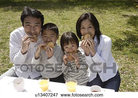 Stock Photo - Portrait of a family eating breakfast in garden. Fotosearch