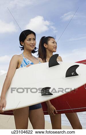 Stock Image - Profile of young women standing with surfboards at beach. Fotosearch