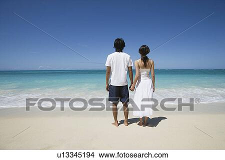 Rear view of a young couple holding hands at beach View Large Photo Image Picture - Rear view of a young couple holding hands at beach. Fotosearch