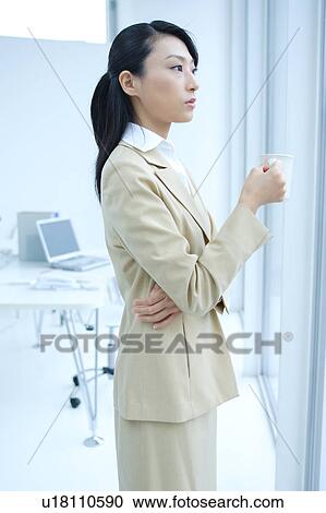 Stock Image - A young businesswoman drinking coffee in office. Fotosearch