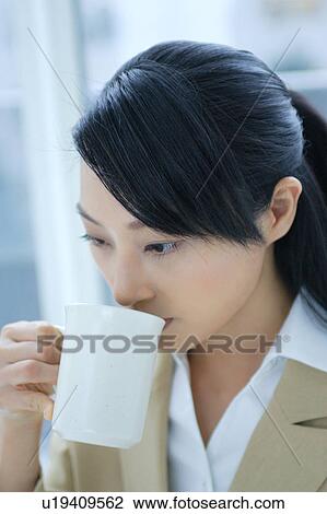 Stock Image - A young businesswoman drinking coffee in office. Fotosearch