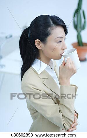 A young businesswoman drinking coffee in office View Large Photo Image Stock Image - A young businesswoman drinking coffee in office. Fotosearch