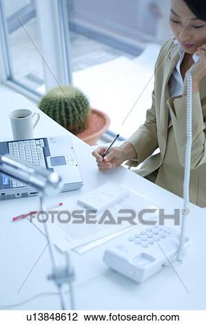 Stock Image - A young businesswoman talking over phone in office. Fotosearch