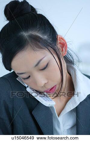 Stock Photo - A young businesswoman talking over mobile phone in office, close-up. Fotosearch