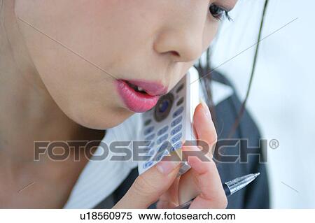 Stock Photography - A young businesswoman talking over mobile phone in office, close-up. Fotosearch