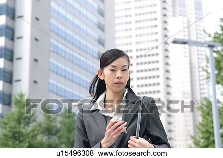 Stock Photo - A young businesswomen looking down with mobile phone in hand. Fotosearch