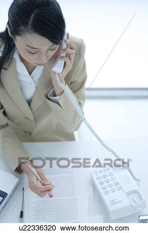 Stock Image - A young woman talking over phone in office. Fotosearch