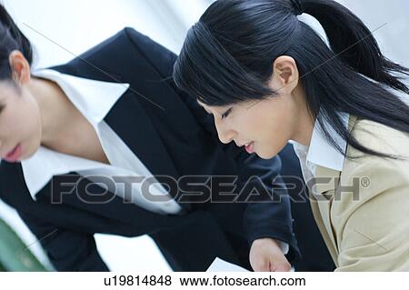 Stock Photo - Two young businesswomen having discussion in office, close-up. Fotosearch