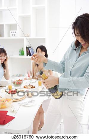 Stock Image - A woman is opening a bottle of champagne. Fotosearch