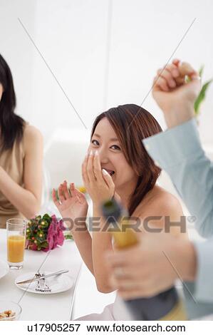 Stock Photo - A woman is opening a bottle of champagne. Fotosearch