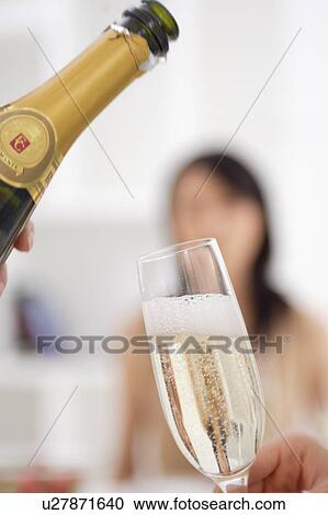 Stock Image - A woman is pouring champagne into glass. Fotosearch
