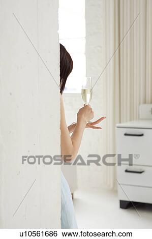 Stock Photograph - A young woman standing with a glass of champagne, rear view. Fotosearch