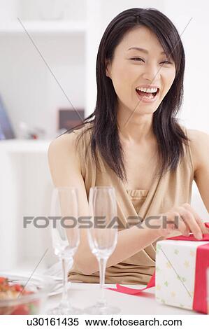 Smiling young woman opening a present View Large Photo Image Stock Photography - Smiling young woman opening a present. Fotosearch