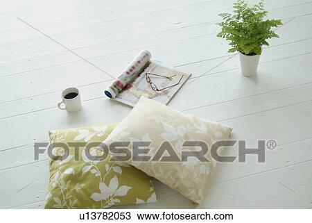 Stock Image - Cushions, magazine, cup of coffee and potted plant on floor. Fotosearch