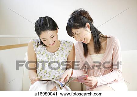 Stock Image - Two young women reading magazine together. Fotosearch