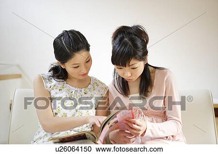 Two young women reading magazine together View Large Photo Image Stock Image - Two young women reading magazine together. Fotosearch