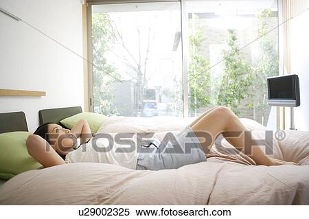 Young woman lying on bed View Large Photo Image Stock Photography - Young woman lying on bed. Fotosearch