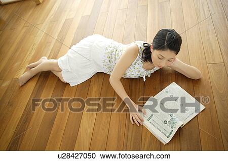 Stock Image - Young woman lying on floor and reading magazine. Fotosearch