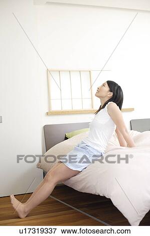 Young woman sitting on bed View Large Photo Image Stock Photo - Young woman sitting on bed. Fotosearch