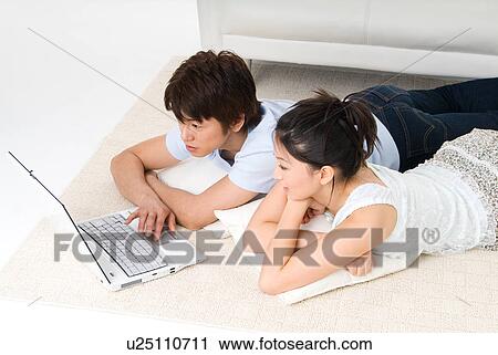 Stock Image - Young couple lying on floor and using computer. Fotosearch
