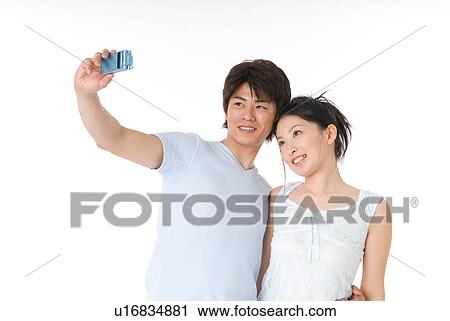 Stock Image - Young couple photographing themselves with cameraphone. Fotosearch