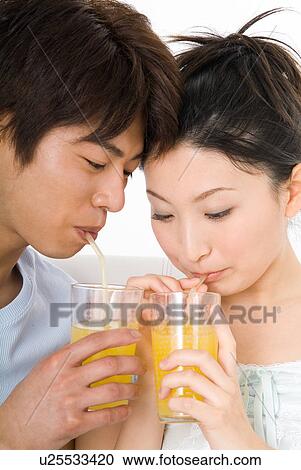 Stock Image - Young couple sitting and drinking orange juice. Fotosearch