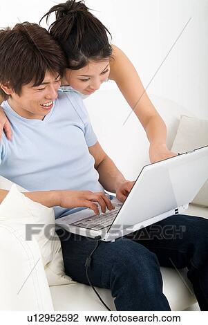 Stock Image - Young couple sitting and looking at laptop computer. Fotosearch