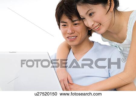 Young couple sitting and looking at laptop computer View Large Photo Image Stock Image - Young couple sitting and looking at laptop computer. Fotosearch