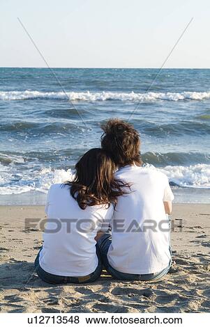Stock Photo - Young couple sitting in a beach. Fotosearch