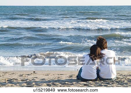 Stock Photo - Young couple sitting in a beach. Fotosearch