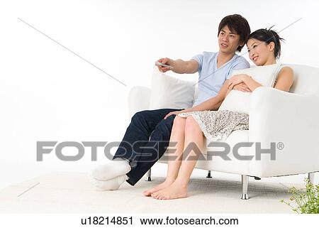 Stock Image - Young couple sitting on sofa and watching television. Fotosearch