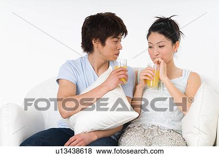Stock Photo - Young couple sitting on sofa and drinking orange juice. Fotosearch