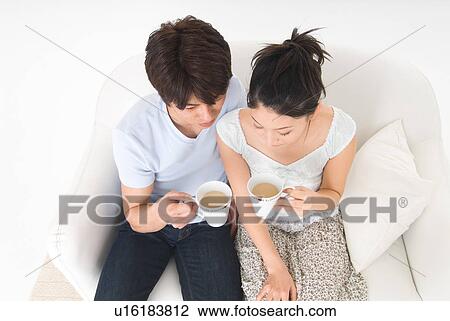 Young couple sitting on sofa holding mug, high angle view View Large Photo Image Stock Image - Young couple sitting on sofa holding mug, high angle view. Fotosearch